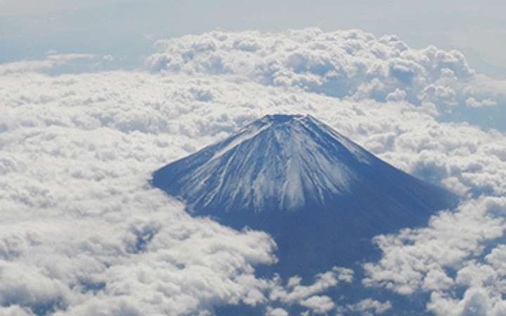 Aerial view of climbers ascending Mount Fuji’s trail with the summit in the distance — capturing Japan’s highest peak during climbing season from above, surrounded by rugged volcanic terrain and clouds