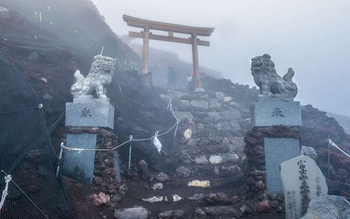Breathtaking view from the summit of Mount Fuji at sunrise, overlooking a sea of clouds and surrounding Japanese landscape — the highest point in Japan and a top destination for climbers and adventurers