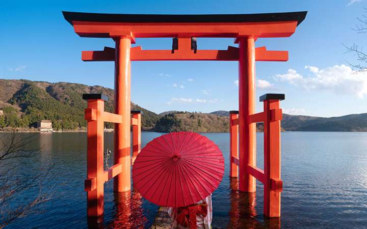 Iconic red torii gate of Hakone Shrine standing in Lake Ashi, surrounded by lush forest and misty mountains, a popular spiritual and scenic spot in Japan.