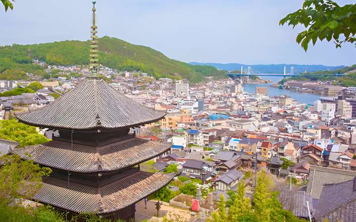 Panoramic view over Onomichi, Japan, featuring a traditional pagoda, coastal townscape, and Seto Inland Sea with Shimanami Kaidō bridge in the distance