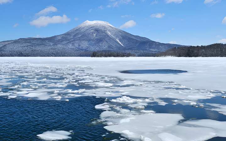 Frozen Lake Akan in Hokkaidō, Japan during winter—scenic volcanic lake framed by snow-covered mountains, known for Ainu culture, marimo algae, and ice fishing activities