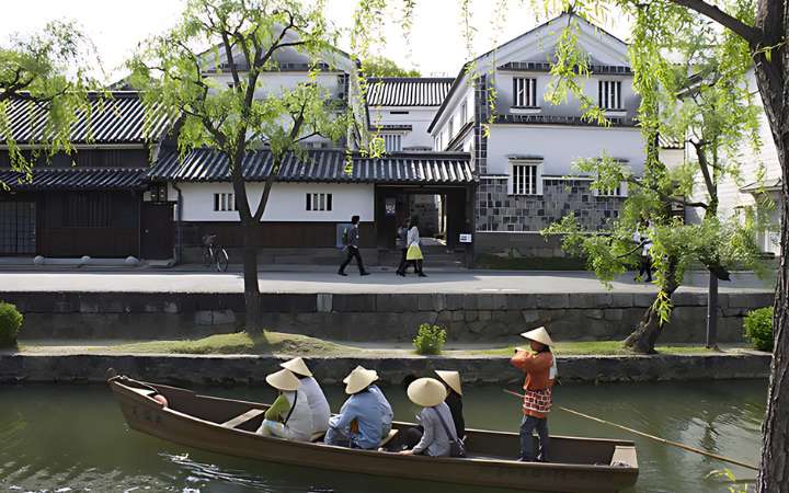 Scenic canal lined with traditional white-walled kura storehouses and willow trees in Kurashiki Bikan Historical Quarter, Japan — a beautifully preserved Edo-period merchant town