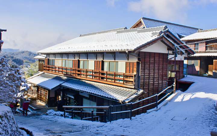 Traditional wooden inn along the Nakasendo Trail in Magome-juku, Japan, covered in winter snow – a historic post town offering scenic mountain views and cultural charm.