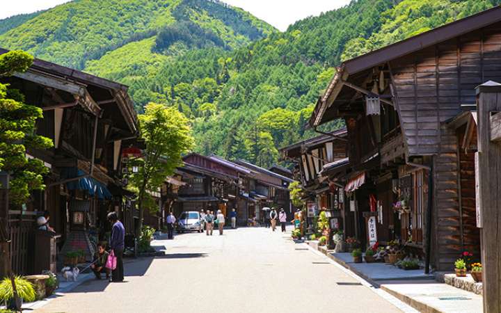 Narai Juku, Traditional wooden buildings lining a historic street in Narai-juku, a preserved Edo-period post town on the Nakasendo Trail in Nagano, Japan, surrounded by lush green