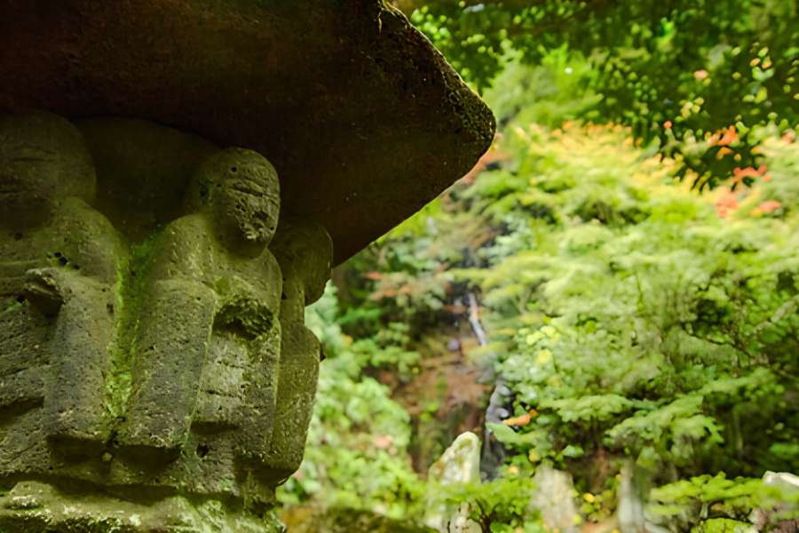 Close-up of traditional carved stone figures on a mossy lantern surrounded by lush forest on Mount Mitaki during the San’in self-guided walking tour.