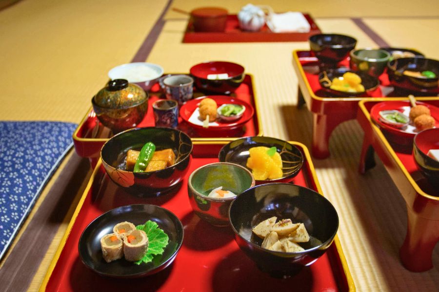 Authentic traditional Japanese food multi-course dinner served on red lacquer trays.